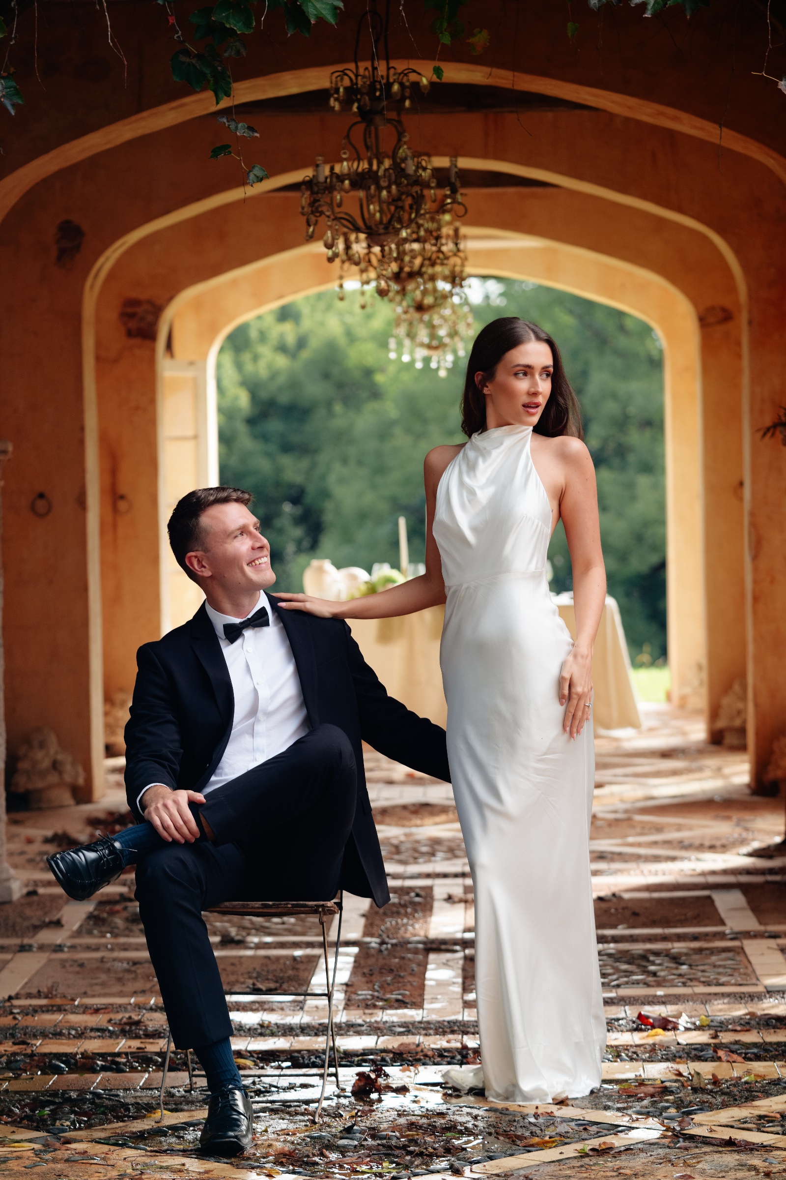 Couple in formal wedding attire posing beneath a series of stone arches.