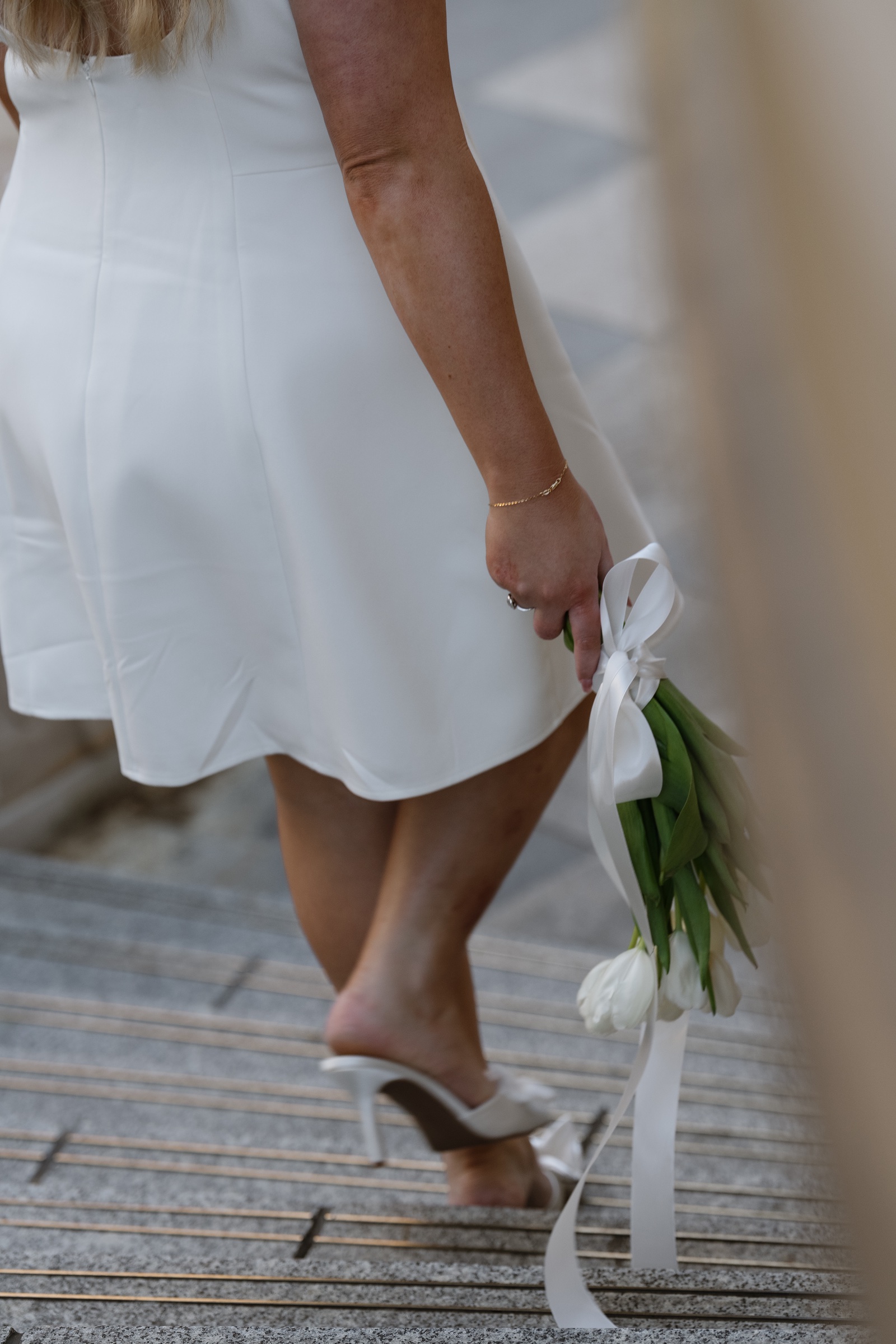 Close-up of a person in a white dress holding white tulips while walking down stairs.