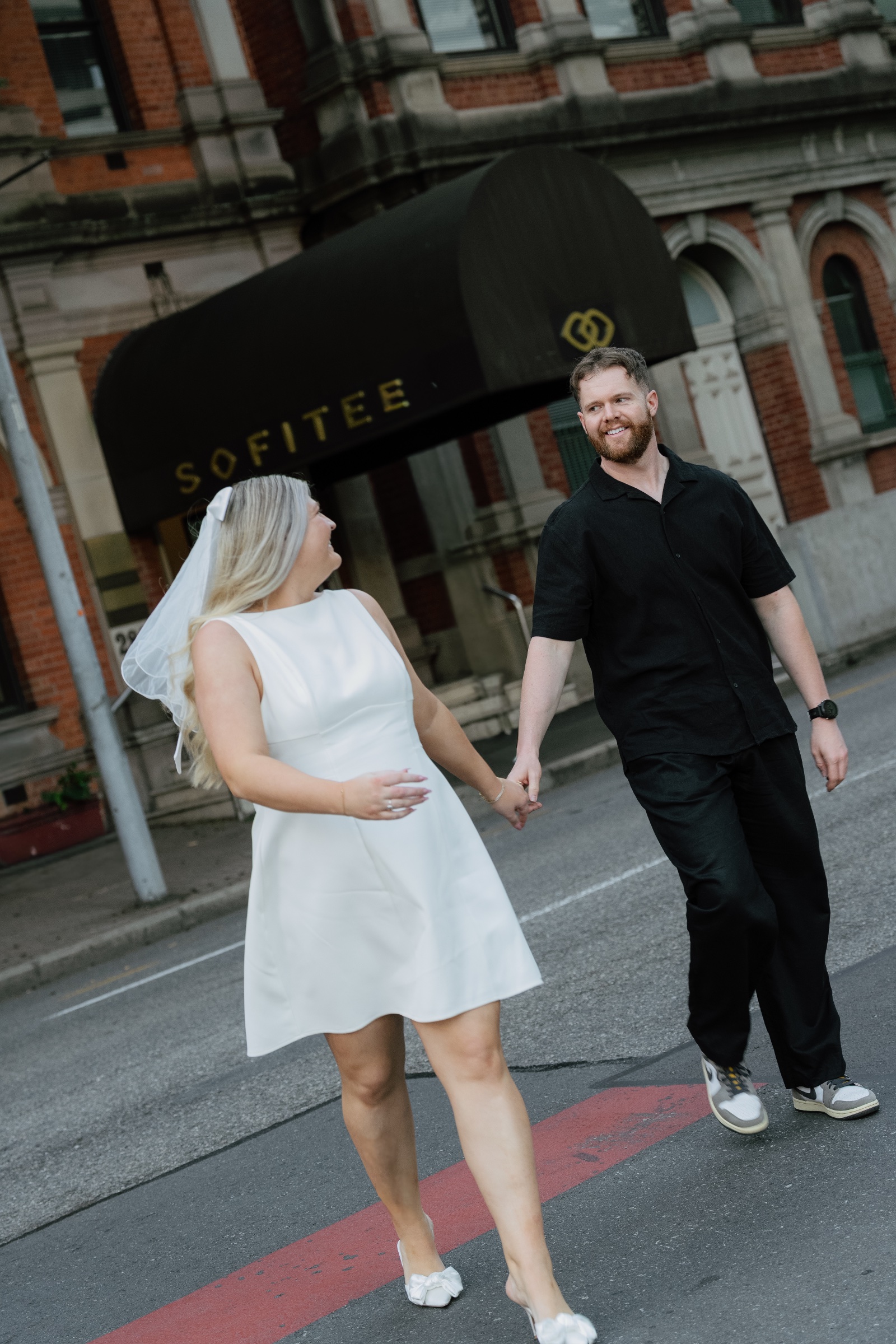 Couple holding hands while crossing a city street in front of a historic building.