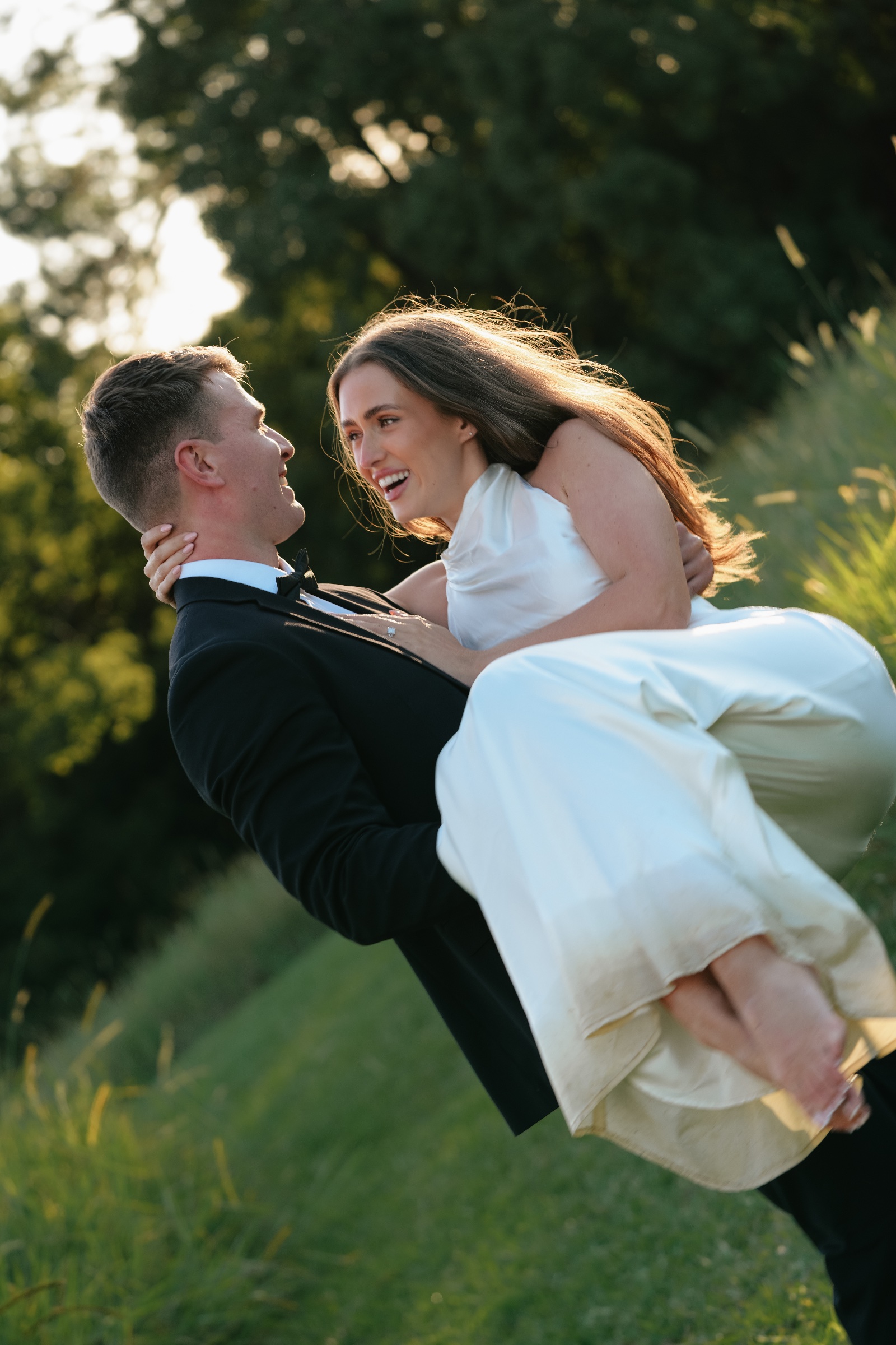Groom carrying the laughing bride through a sunlit garden.