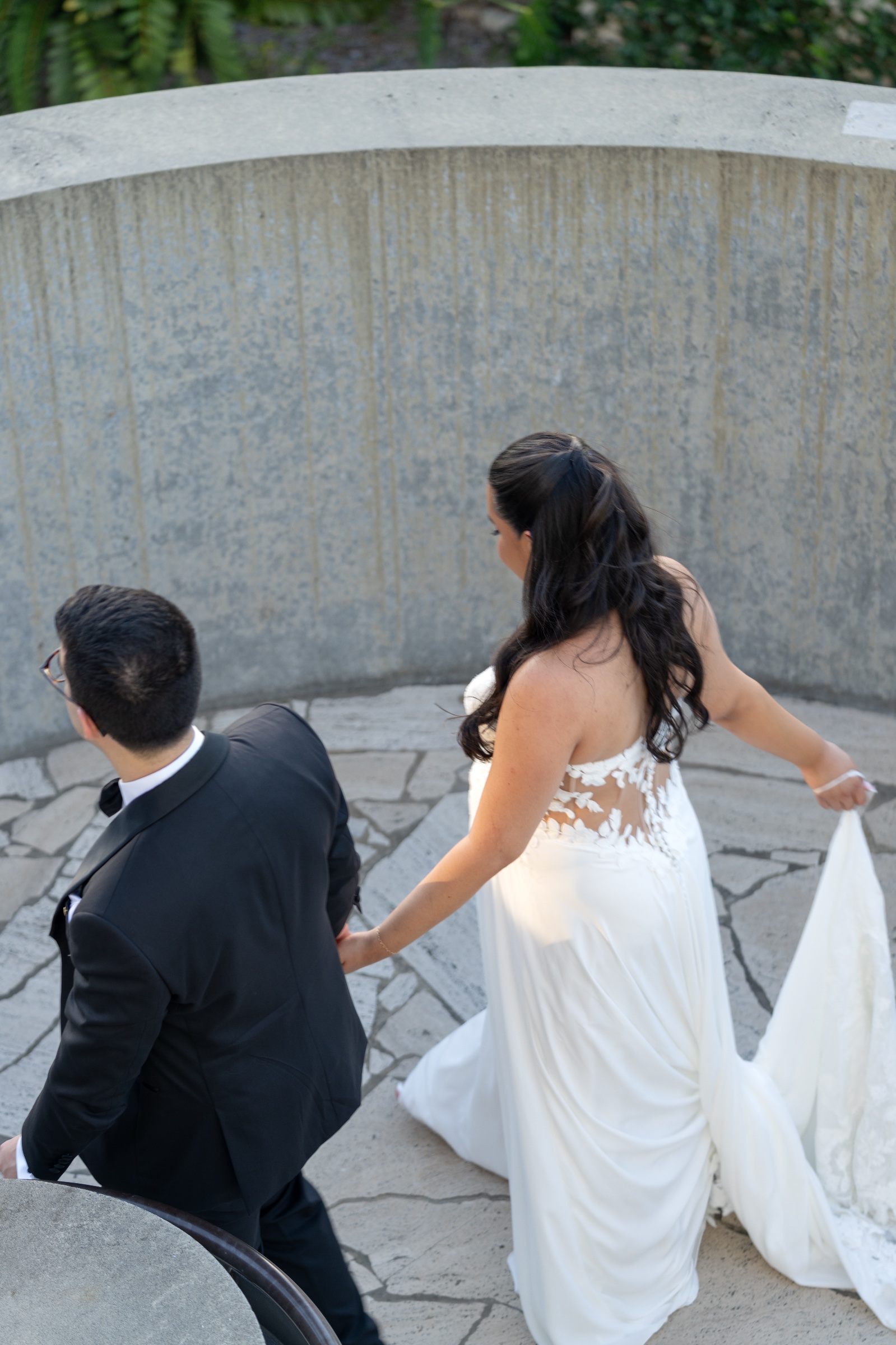 Bride holding her train while following the groom around a curved outdoor stairway.