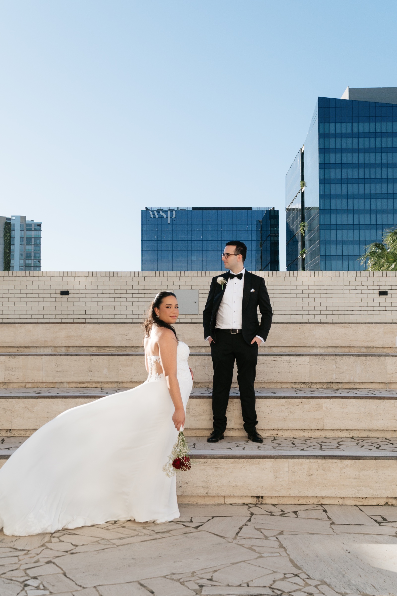 Bride and groom on outdoor stone steps, with the bride’s train spread beside her.