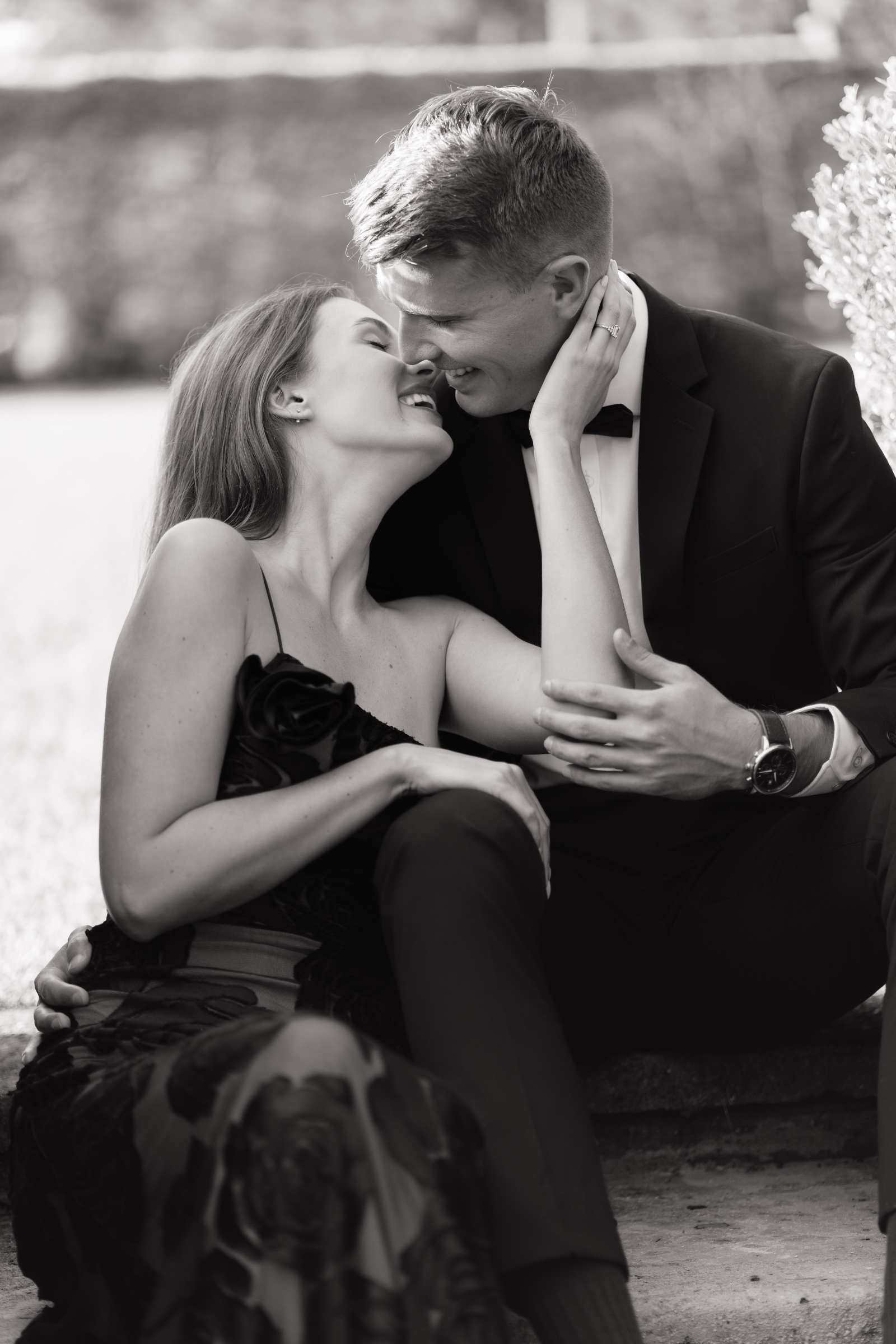 Black and white portrait of a seated couple kissing while holding hands.