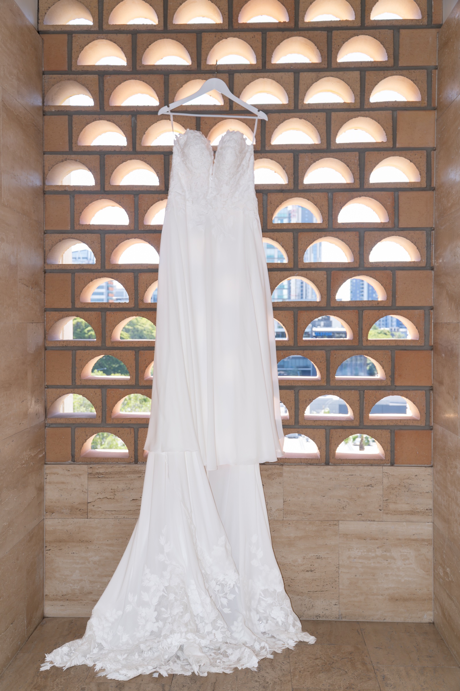 White wedding dress hanging against a patterned wall of arched openings.